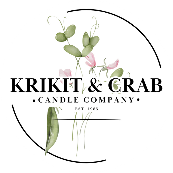 "Logo for Krikit & Crab Candle Company featuring elegant black serif text over a watercolor illustration of green leaves and soft pink flowers. The design is enclosed in a minimalistic circular frame with black accents and includes the text 'Candle Company' and 'Est. 1985' beneath the main brand name."