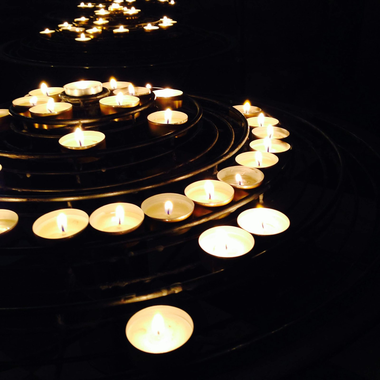 Softly lit candles arranged in a spiral create a warm glow against a dark background, evoking tranquility.
