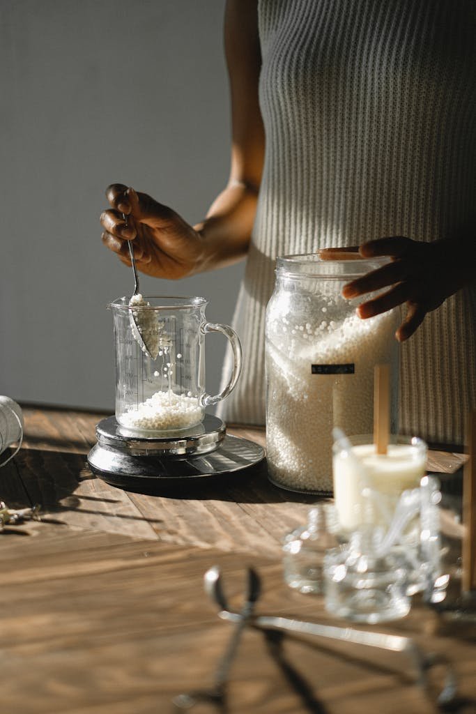 African American woman carefully measures wax granules for candle making in a cozy studio setting.