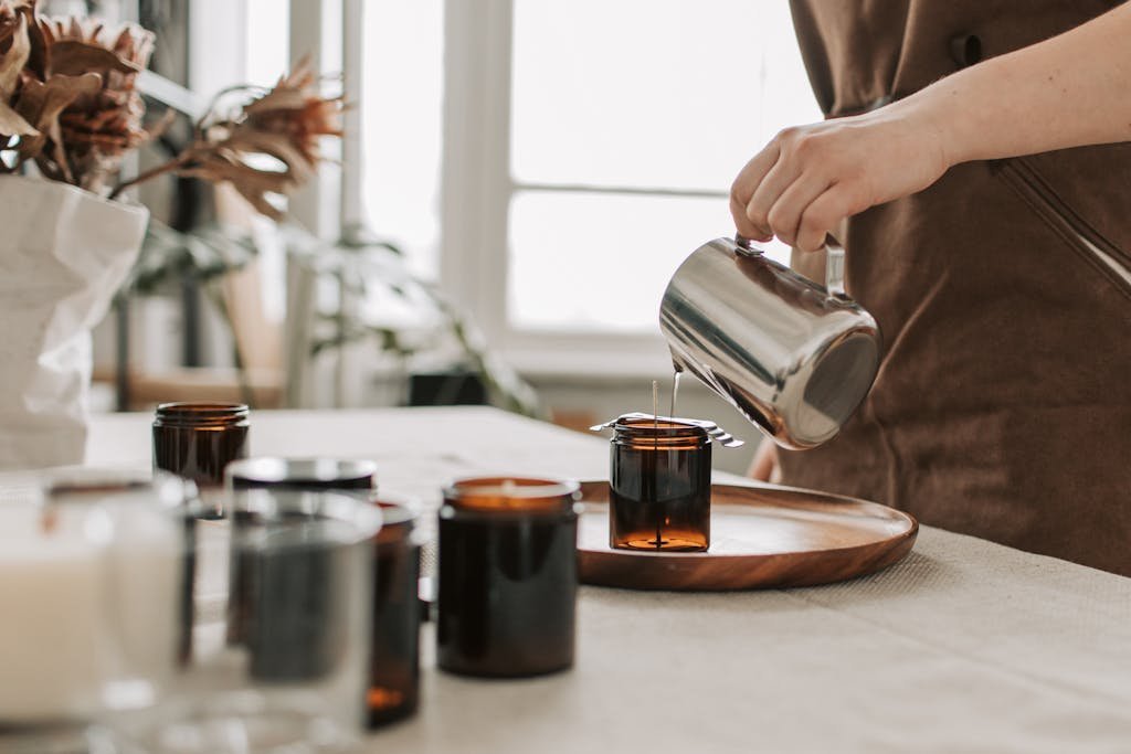 Close-up of a woman pouring wax into jars for handmade candle making.