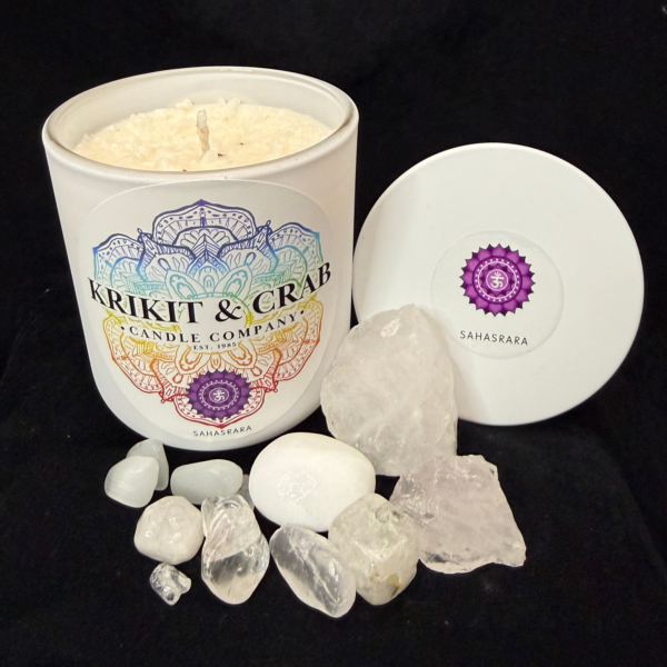 Krikit & Crab Candle Company Sahasrara (Crown Chakra) candle in a white vessel with a purple chakra symbol on the lid. The candle is surrounded by white quartz and clear crystal stones against a black background.