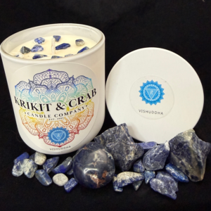 “Krikit & Crab Candle Company Vishuddha (Throat Chakra) candle featuring blue lapis lazuli chips on top. The candle is displayed with lapis stones and raw blue crystals, with the blue throat chakra symbol on the lid.”
