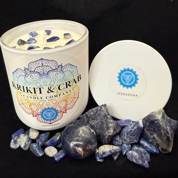 “Krikit & Crab Candle Company Vishuddha (Throat Chakra) candle featuring blue lapis lazuli chips on top. The candle is displayed with lapis stones and raw blue crystals, with the blue throat chakra symbol on the lid.”
